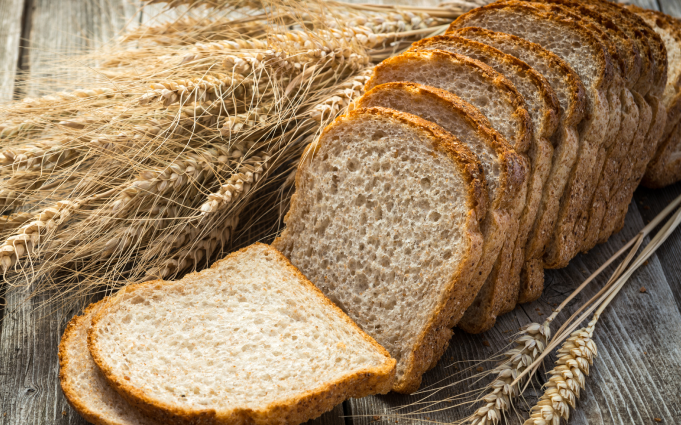 Sliced whole grain bread rests on a wooden table, accompanied by golden wheat stalks in the background.