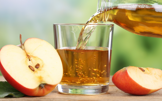 كوب مملوء بعصير التفاح من زجاجة، وبجانبه شرائح التفاح الأحمر على سطح خشبي.