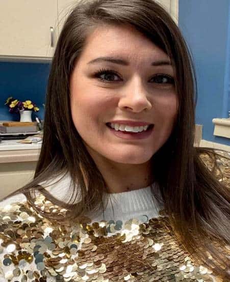 A woman with long brown hair, a gold sequin top, and a bright smile is an office’s Cheers for Peers Breastfeeding Peer Counselor.