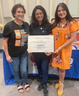 Three women stand together, smiling, as the January 2026 Cheers for Peers Breastfeeding Peer Counselors award is presented.